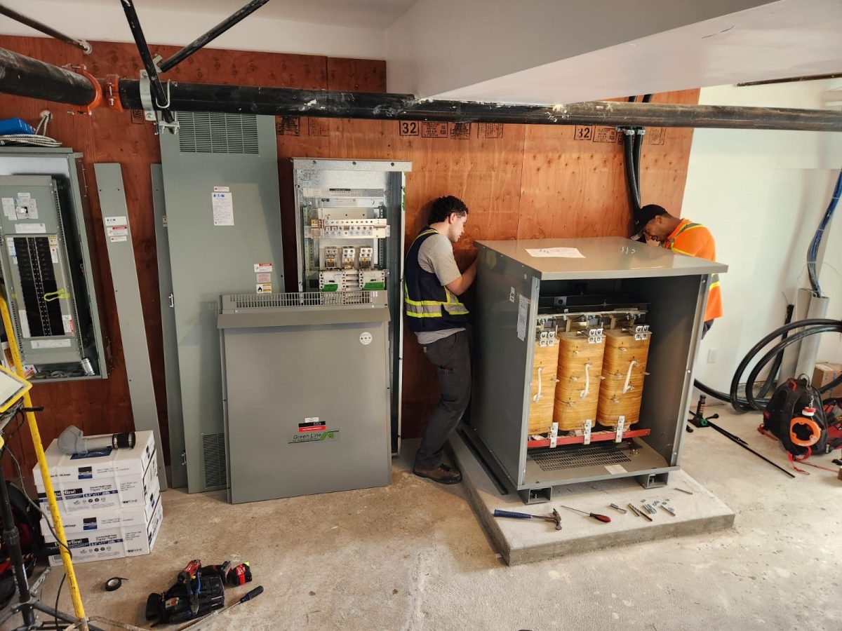 electricians installing a large electrical transformer, likely for a commercial or industrial building